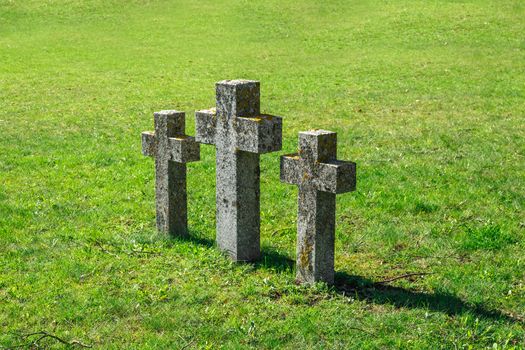Close up side view of three stone cross signs in a meadow area, on green grass background.