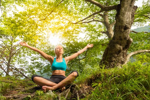 Relaxed woman enjoying freedom and life in beautiful natural environment. Blissful girl raising arms, feeling free, relaxed and happy. Concept of freedom, happiness, enjoyment and natural balance.