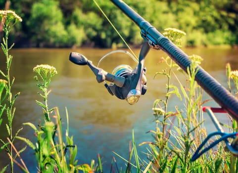 On the banks of the beautiful river above the water feeder installed - English fishing tackle for catching fish comfortable with the rod and the reel.