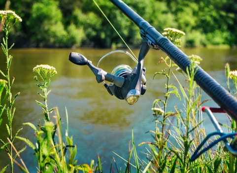 On the banks of the beautiful river above the water feeder installed - English fishing tackle for catching fish comfortable with the rod and the reel.