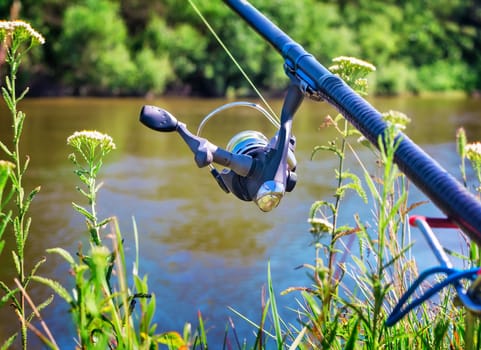 On the banks of the beautiful river above the water feeder installed - English fishing tackle for catching fish comfortable with the rod and the reel.