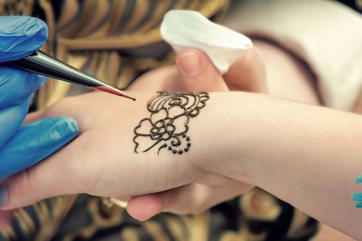 Tool for tattoos tattoo artist make a drawing on the back of the hand of the girl.