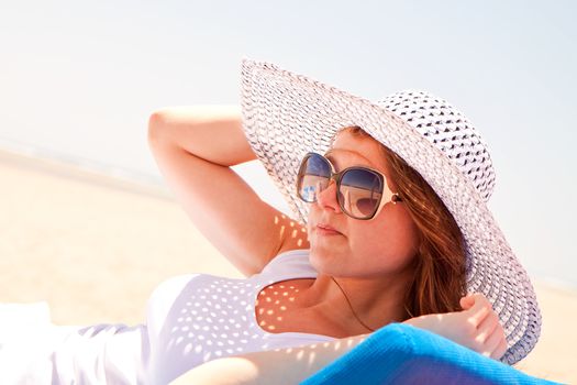 Young woman in a hat relaxes on a lounger on the beach