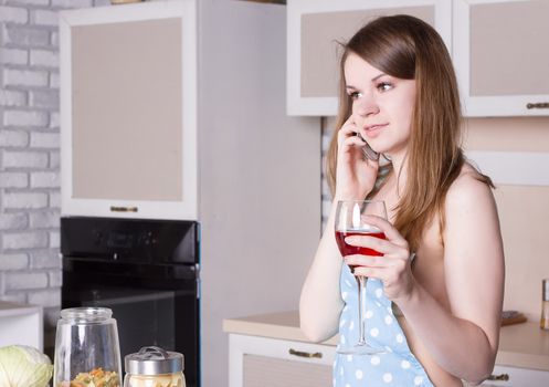 girl in the kitchen wearing an apron over his naked body with a glass of wine