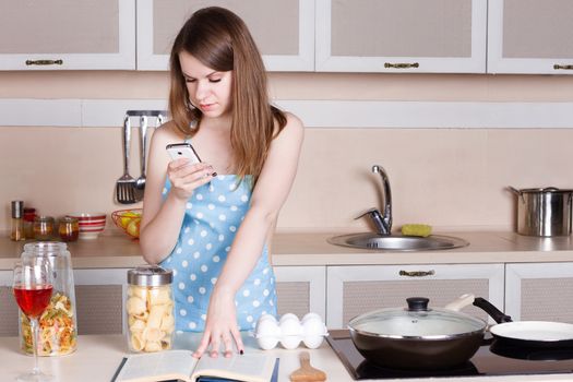  girl in the kitchen wearing an apron over his naked body prepares and looks into the phone