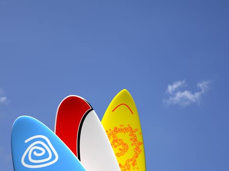 A set of surf boards vertically positioned with a blue sky and some clouds on the background