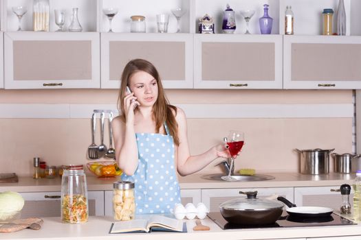 girl in the kitchen wearing an apron over his naked body with a glass of red wine on the phone. Horizontal framing