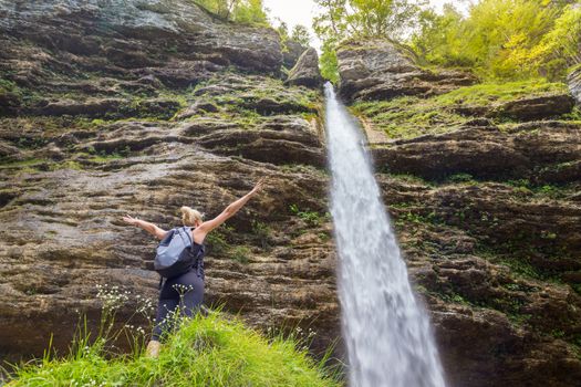 Female hiker raising arms inhaling fresh air, feeling relaxed and free in beautiful natural environment under Pericnik waterfall in Vrata Valley in Triglav National Park in Julian Alps, Slovenia.