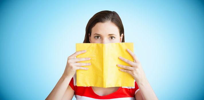 Student covering face with book in library against blue background with vignette