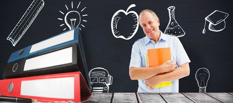 Mature student holding notebooks against blackboard