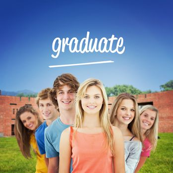 The word graduate and smiling group standing behind one another at various angles against students using laptop in lawn against college building