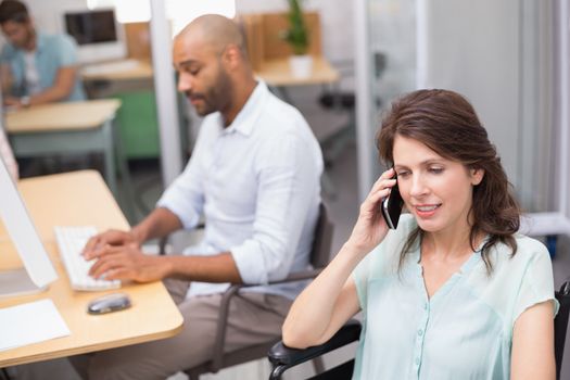 Smiling businesswoman in wheelchair on the phone in front of his colleague in the office