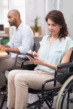 Businesswoman in wheelchair texting on phone in the office