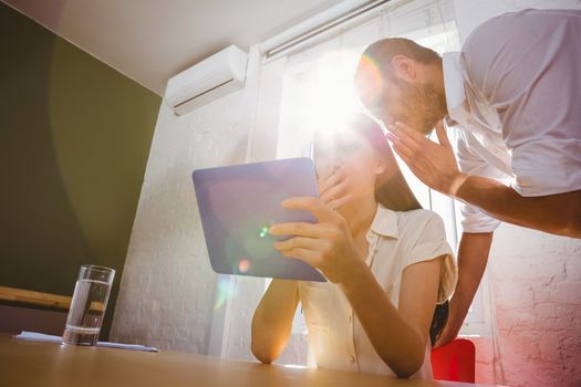 Young man whispering secret into female friends ear while using digital tablet