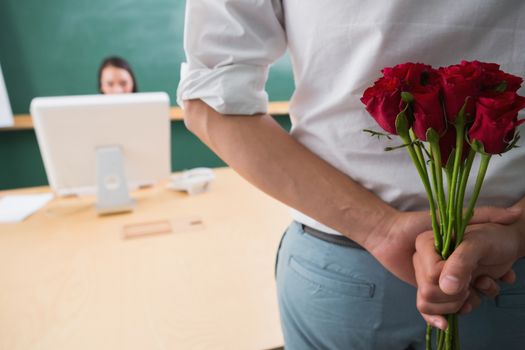 Close up of man hiding bouquet in front of businesswoman at office desk