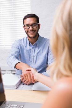 Young businessman shaking hands with woman during interview in office