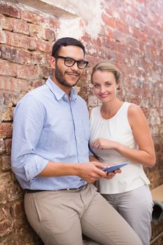 Two young business people text messaging against brick wall in office