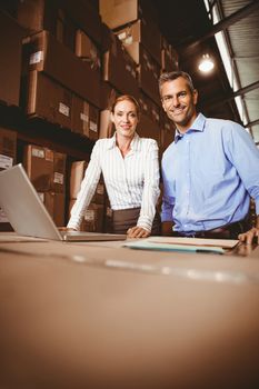 Portrait of warehouse manager and colleague using laptop