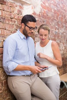 Two young business people text messaging against brick wall in office