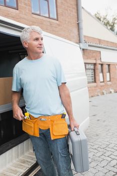 Man with tool belt and briefcase standing by delivery van