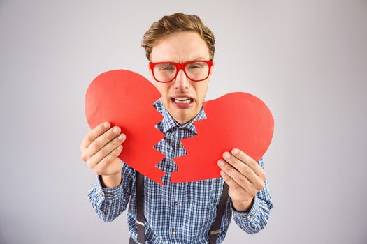 Geeky hipster holding a broken heart on grey background