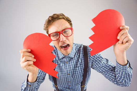 Geeky hipster holding a broken heart on grey background