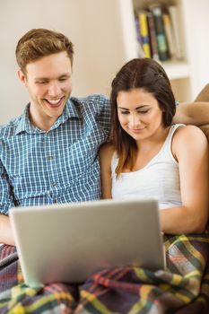 Happy young couple relaxing on the couch with laptop at home in the living room