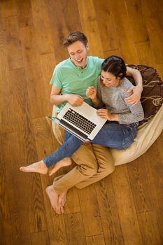 Cute couple using laptop on beanbag at home in the living room