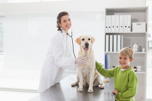 Smiling vet examining a dog with its owner in medical office