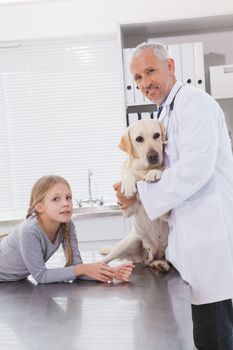 Smiling vet examining a dog with its owner in medical office