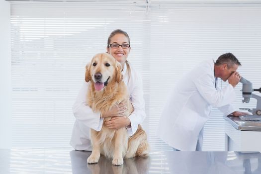 Smiling doctor holding a labrador as co worker checks tests