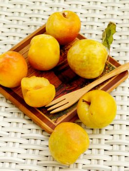 Arrangement of Ripe Yellow Plums on Wooden Plate with Wooden Fork closeup on Wicker background