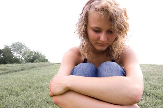 Young depressed girl sitting on a grass in park.