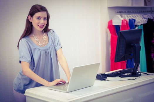 Shop worker using laptop by the till in fashion boutique