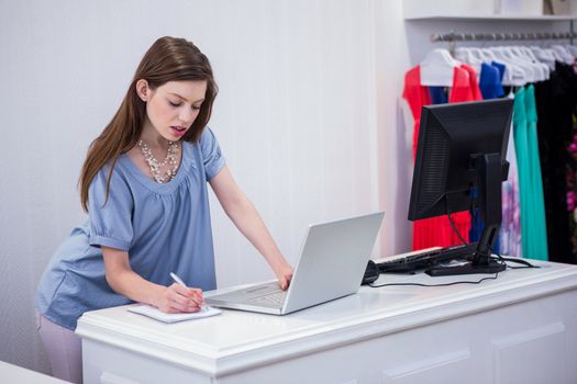 Shop worker using laptop by the till in fashion boutique