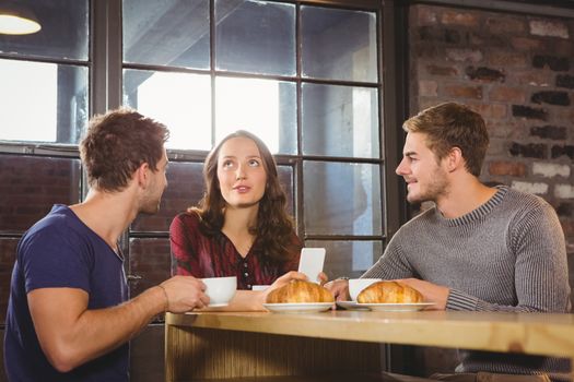 Friends talking and enjoying coffee and croissants at coffee shop