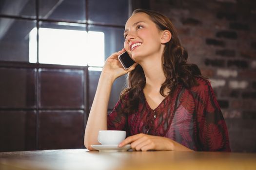 Smiling brunette having coffee and phoning at coffee shop