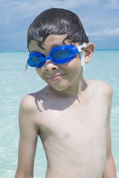 Closeup of handsome Caucasian boy wearing blue swim goggles and dripping wet from swimming in tropical sea under sunny sky while on summer vacation