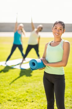 Portrait of smiling sporty woman in front of friends doing exercises in parkland