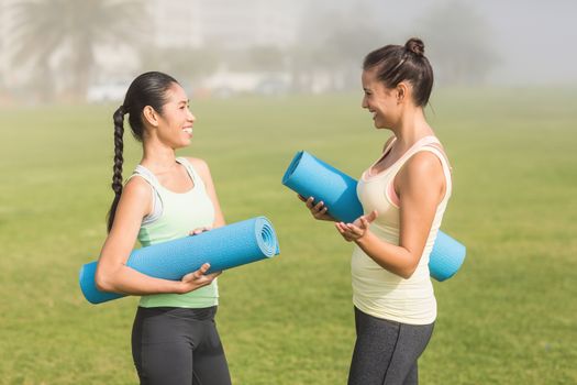 Sporty women with exercise mats chatting in parkland