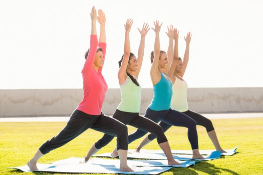 Smiling sporty women doing warrior pose in yoga class in parkland