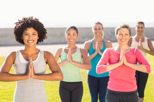 Portrait of smiling sporty women doing prayer position in yoga class in parkland