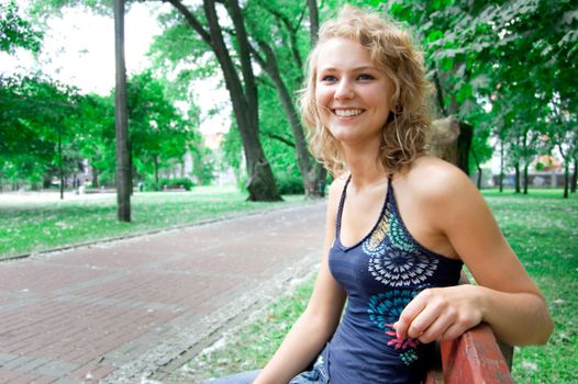 Young beautiful girl sitting on a park bench and smiles.