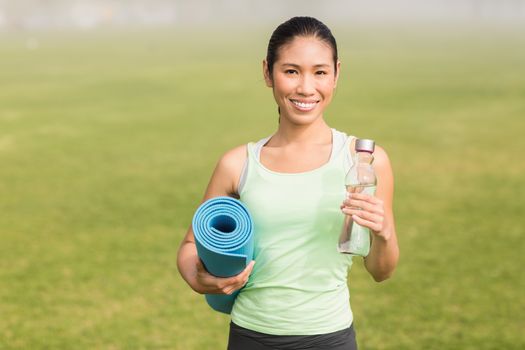 Portrait of sporty woman holding exercise mat and water bottle in parkland