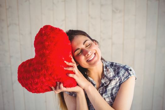Pretty hipster holding heart pillow on wooden planks background