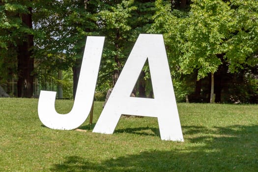 German Yes (Ja) written with upper case letters, on a green meadow with trees in the background