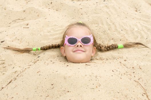 Funny five-year girl with glasses on a beach strewn on his head in the sand