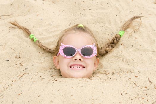 Funny five-year girl with glasses on a beach strewn on his head in the sand