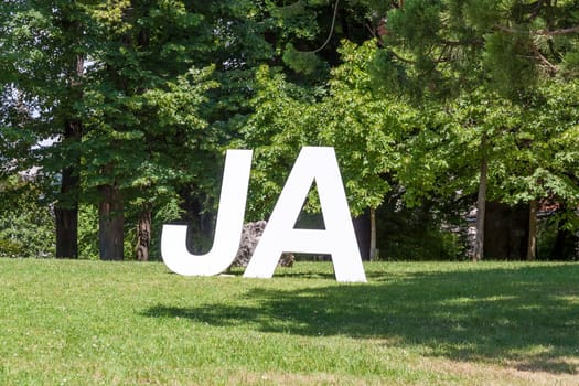 German Yes (Ja) written with upper case letters, on a green meadow with trees in the background