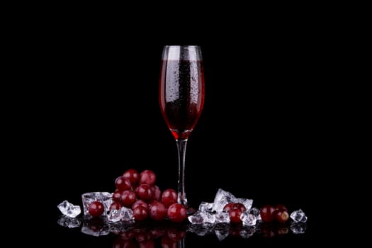 Red grape with glass of champagne on black background